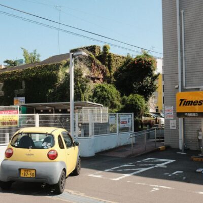 Yellow car in an urban Japan parking lot with ivy-covered building.