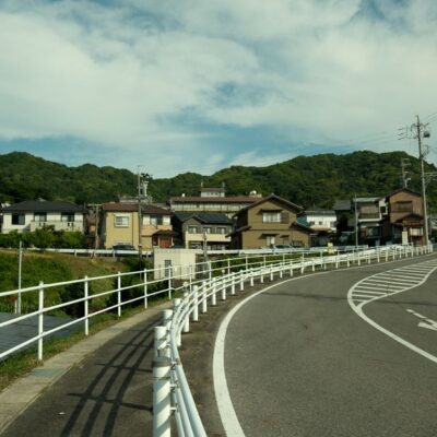 Curved road through suburban Gamagōri, Japan, with traditional houses and lush hills.