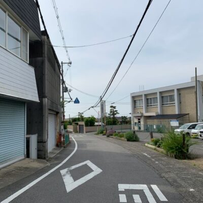 A tranquil suburban street in Osaka, Japan, featuring urban architecture and parked cars.