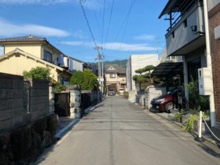 View of a calm residential street in Ashiya, Japan, with houses and parked cars under a blue sky.