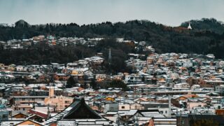 Snow-covered townscape in Japan showcasing traditional architecture and forested hills.