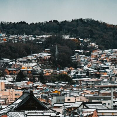 Snow-covered townscape in Japan showcasing traditional architecture and forested hills.