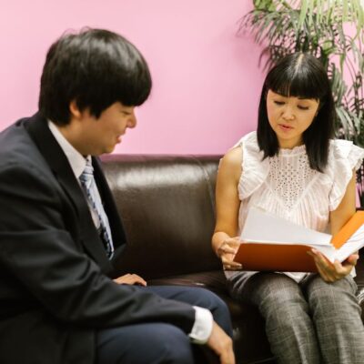 Two business professionals discussing documents on a sofa in an office setting.