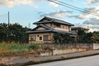 A serene view of a traditional Japanese house with a slate roof set against a cloudy blue sky.