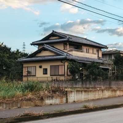 A serene view of a traditional Japanese house with a slate roof set against a cloudy blue sky.
