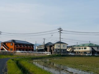 A peaceful Japanese suburban scene with traditional houses and a rice field.