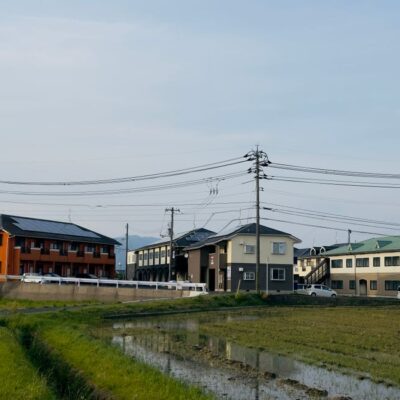 A peaceful Japanese suburban scene with traditional houses and a rice field.